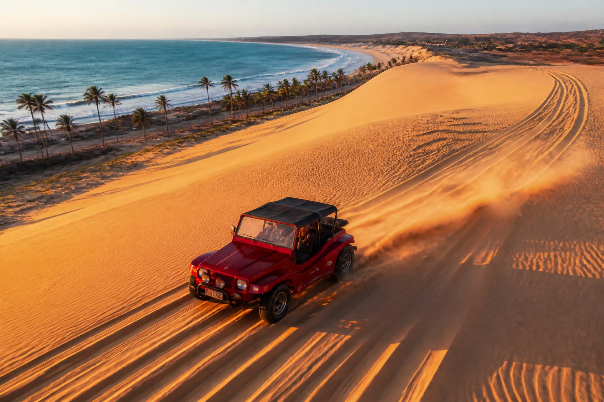 Buggy vermelho descendo duna dourada em Aquiraz ao pôr do sol